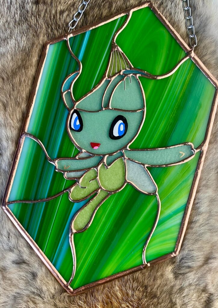 I’m a stained glass artist and this is my Celebi! Swipe to see her glow in the dark! I hand painted the face details as well!!